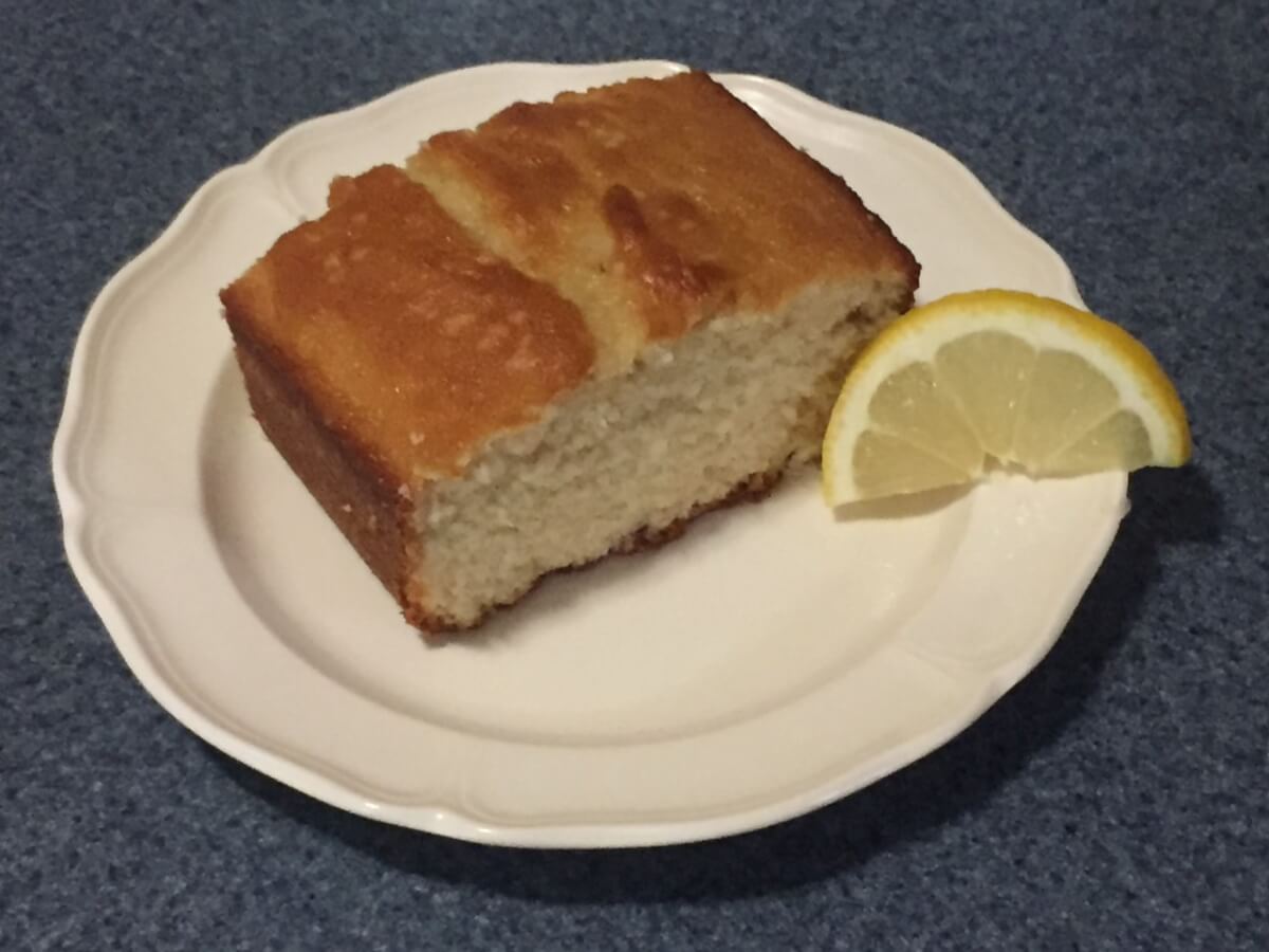 Part of a baked loaf of bread sits on a plate with a lemon slice.
