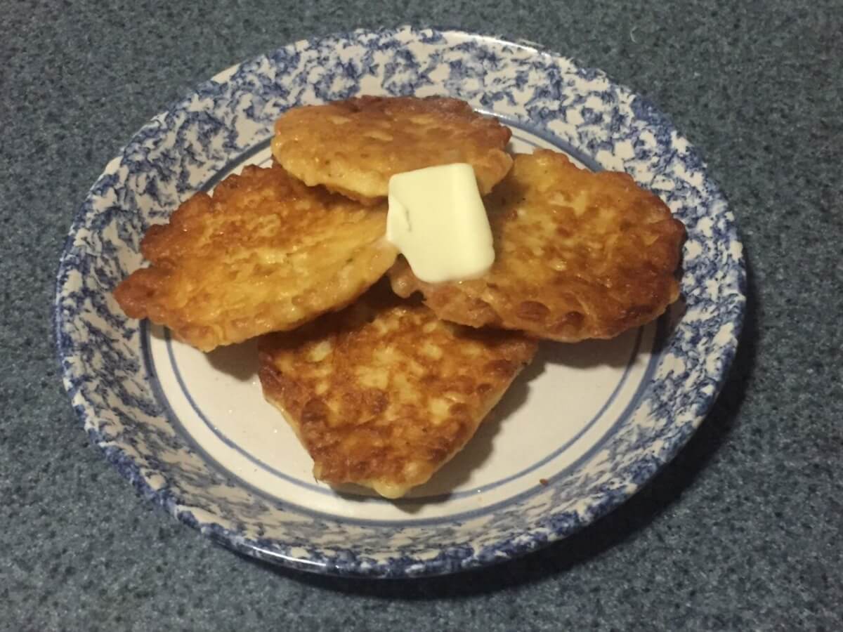 Browned corn fritters sit on a plate with butter on top.