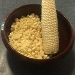 Tazón de granos de maíz con una mazorca.