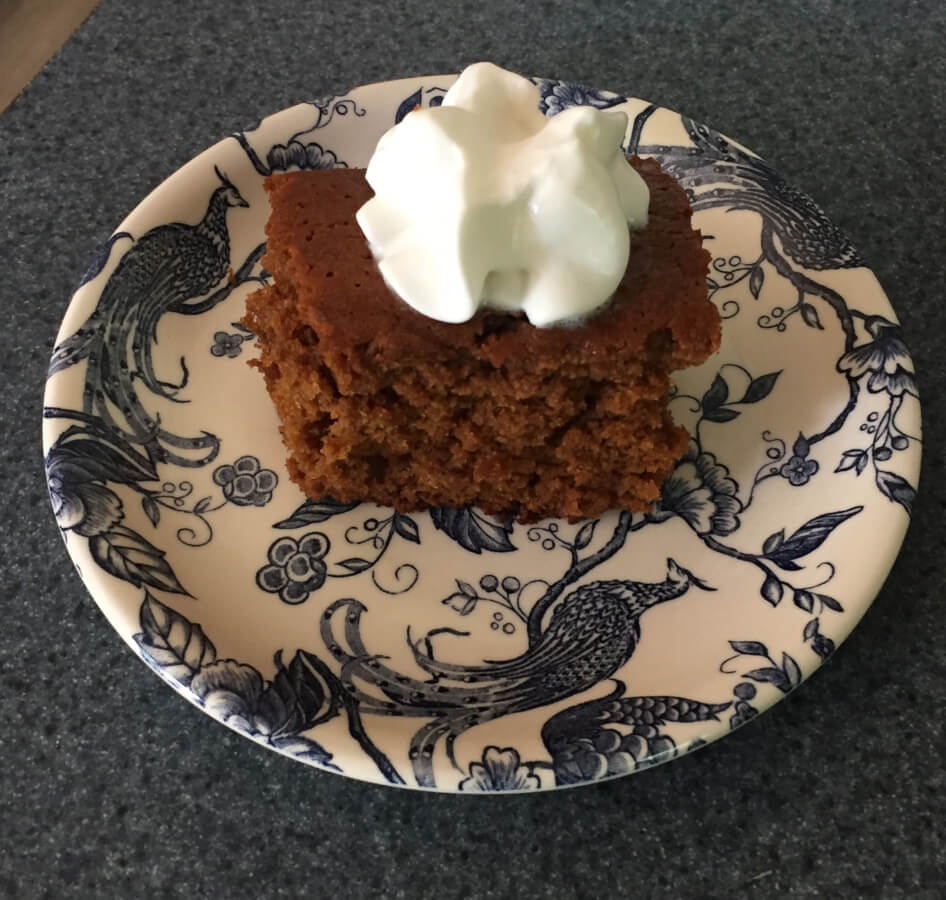 Baked gingerbread cake slice on a plate topped with whipped cream.