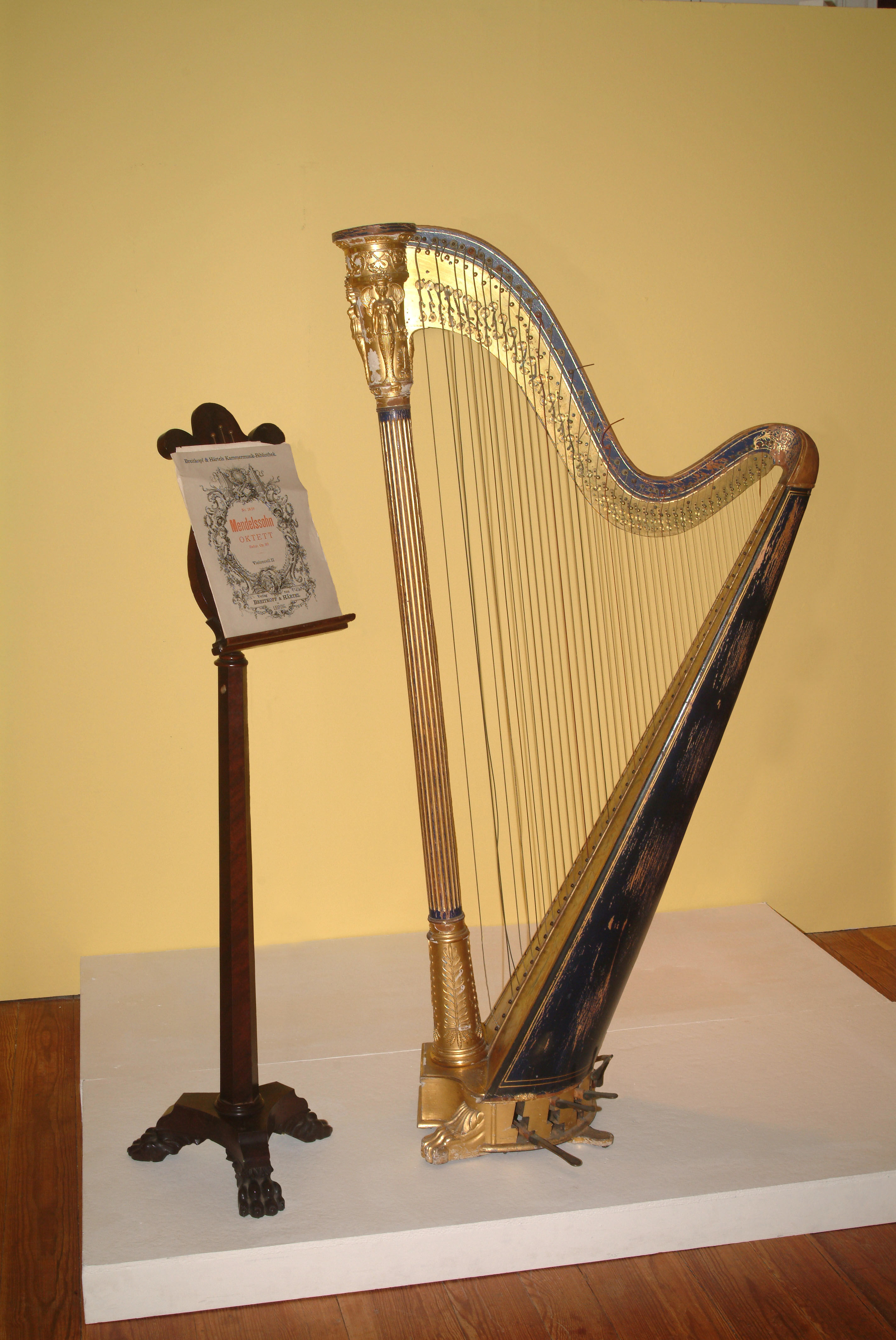 A wooden music stand with sheet music stands next to a large harp.