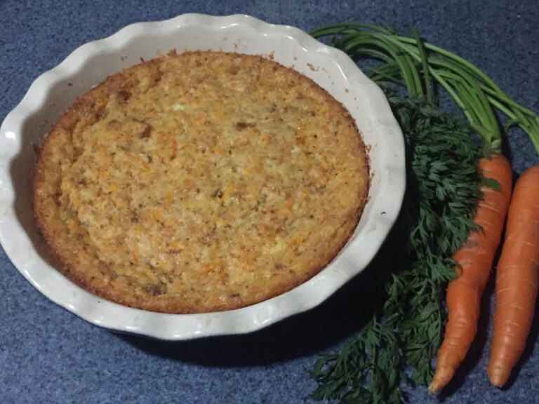 A baked carrot pudding in a baking dish. Two whole carrots sit to the right.
