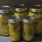 Five glass jars filled with yellow mustard pickles and seasonings.