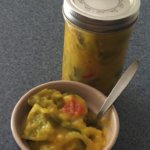 A glass jar of sweet mustard pickles sits next to a bowl of sweet mustard pickles.