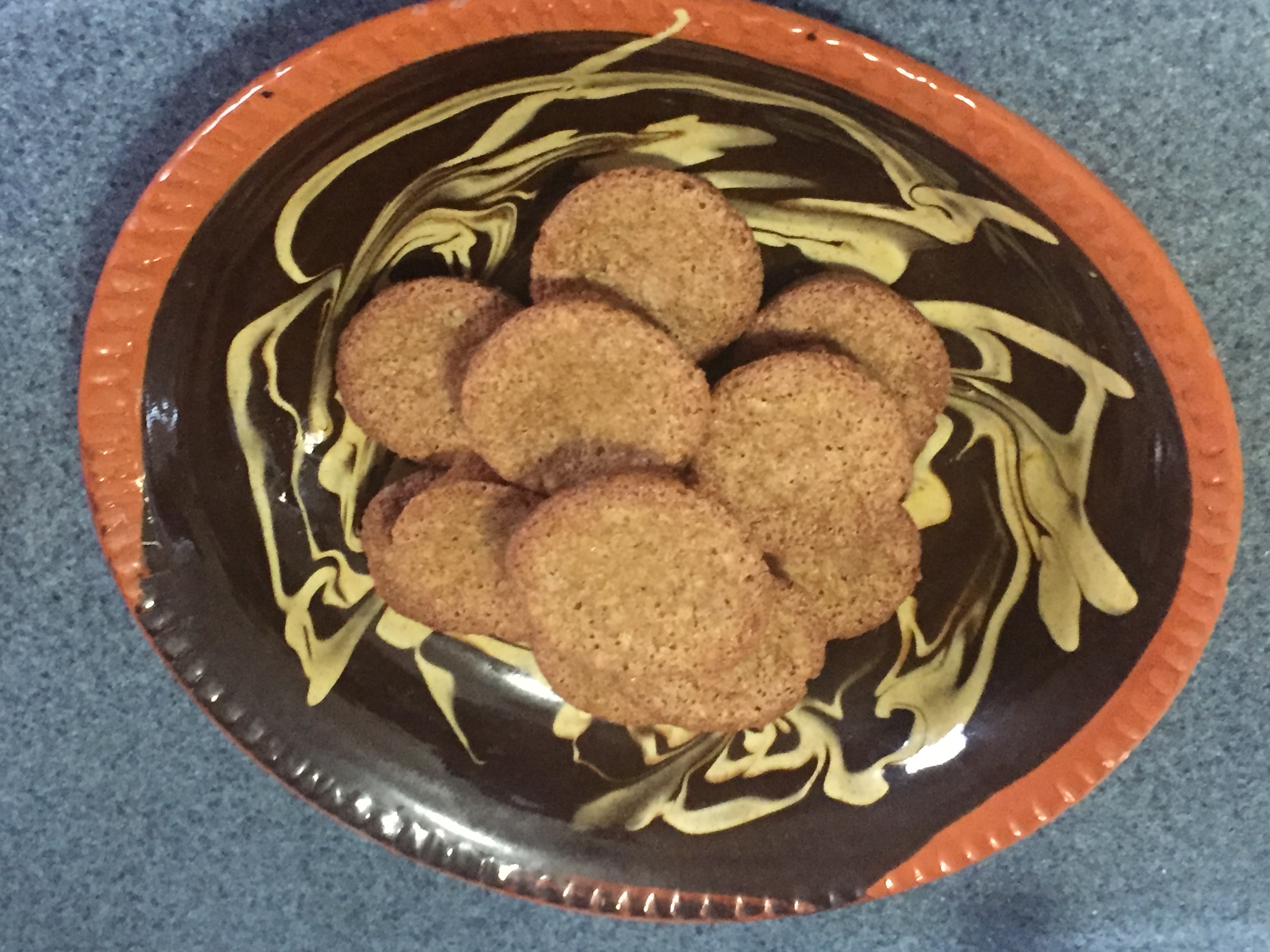 Eleven baked small nut cakes are stacked on a black and orange plate with yellow decorative swirling.