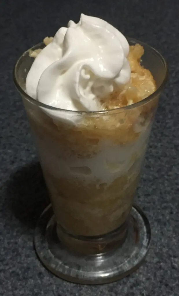 A serving of apple pudding in a tall parfait glass layered with whipped cream.