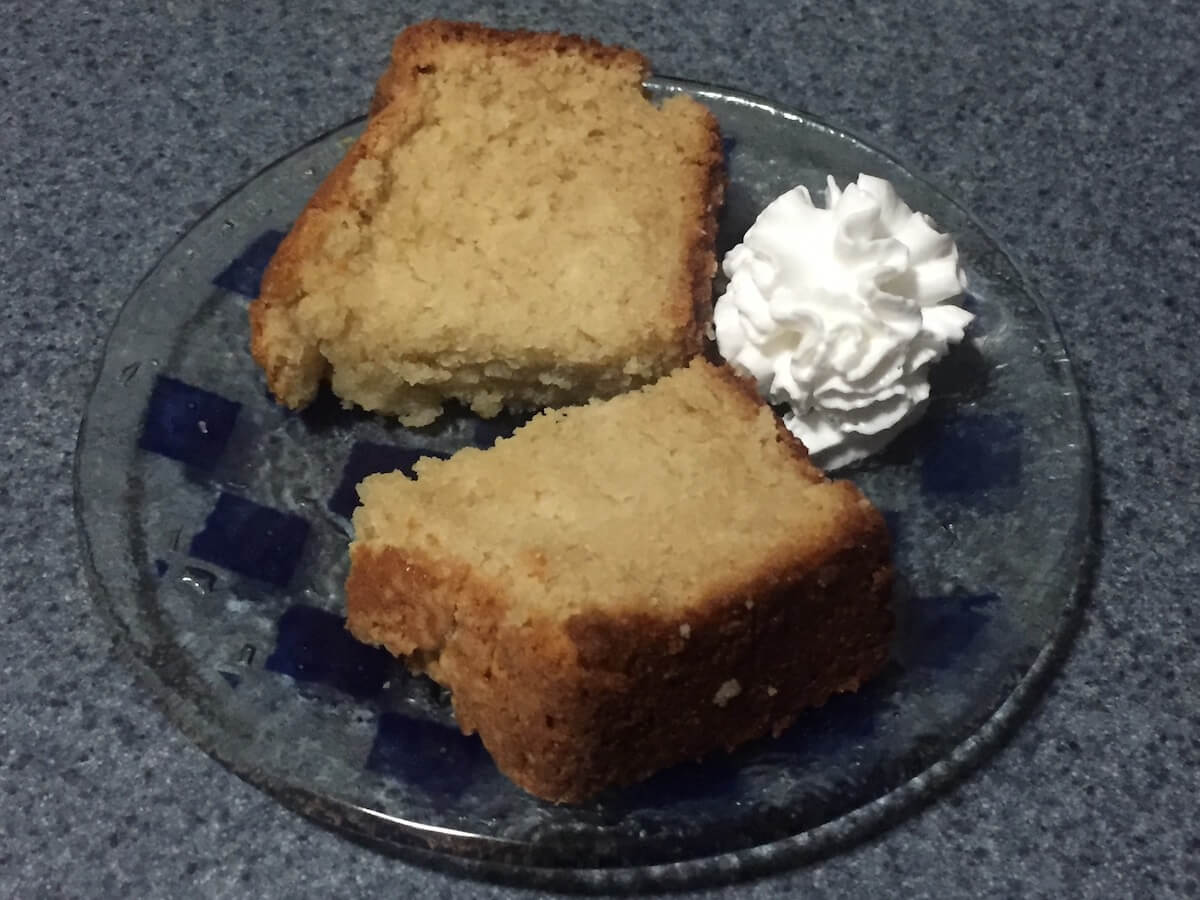 Two slices of baked cider cake sit on a plate with whipped cream to the side.