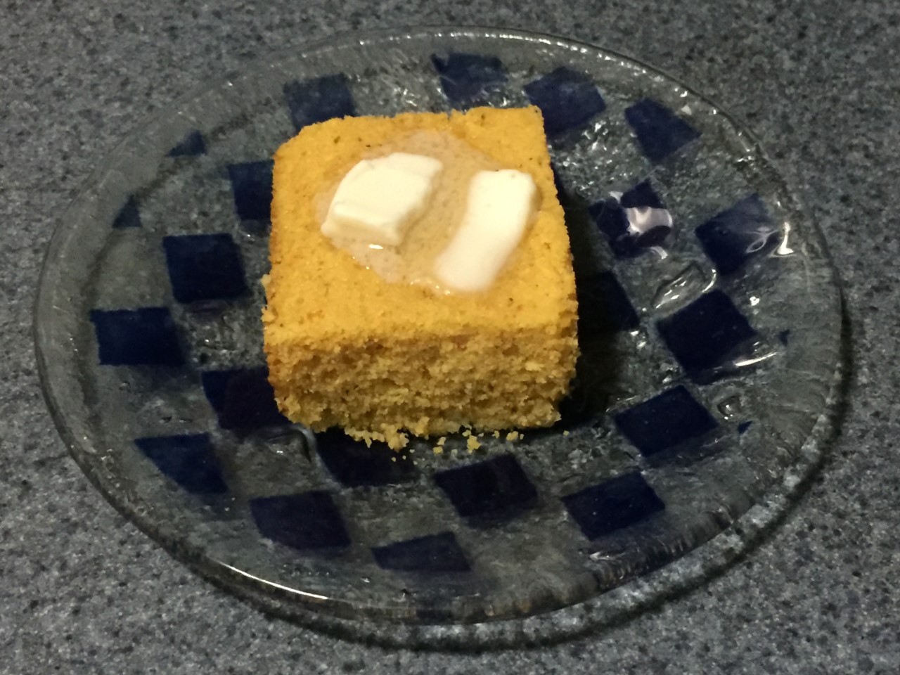 Una rebanada cuadrada de pastel de maíz amarillo con mantequilla derretida por encima.