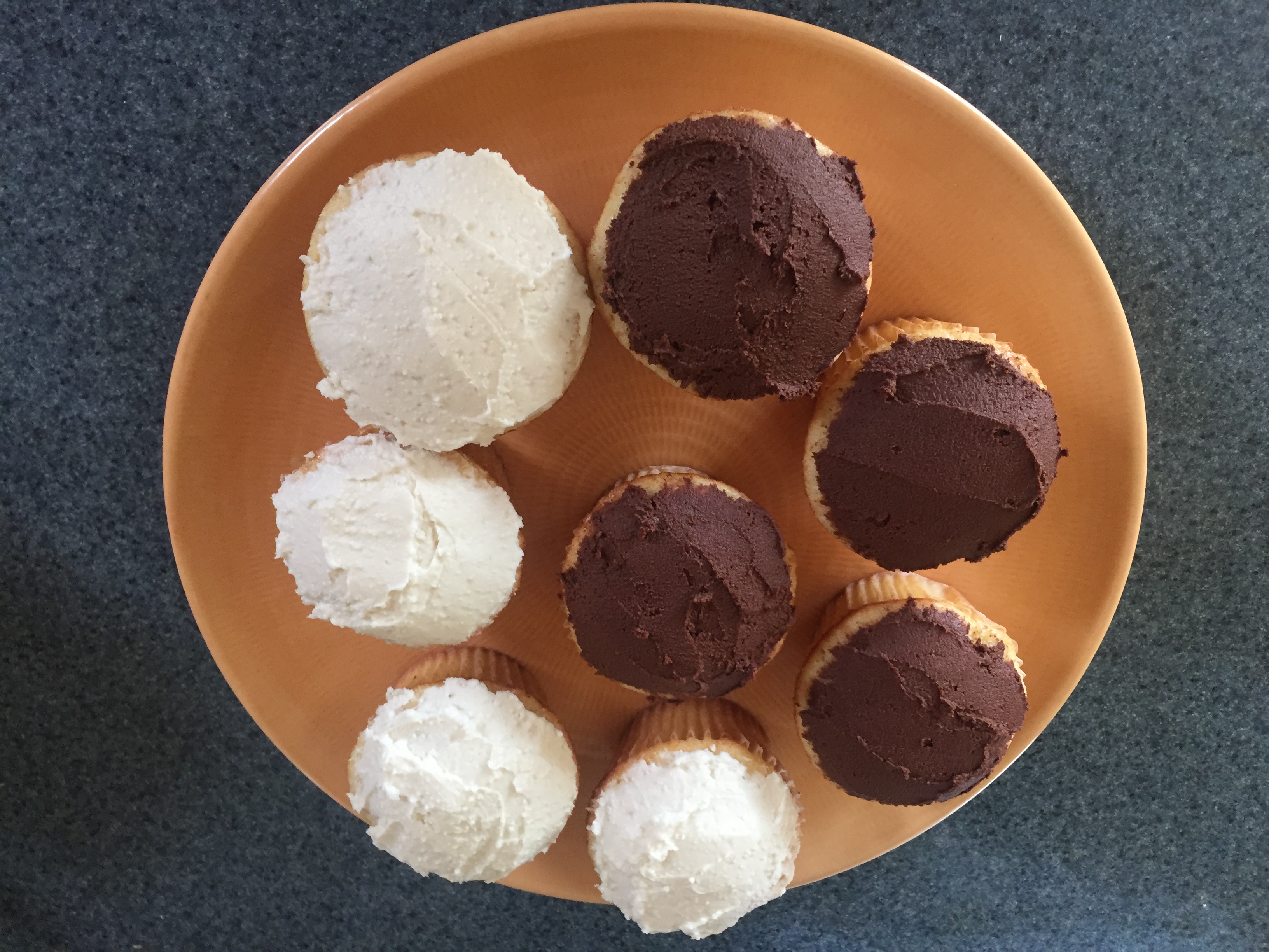 Cuatro cupcakes con glaseado de chocolate y cuatro cupcakes con glaseado de vainilla dispuestos en un plato naranja.