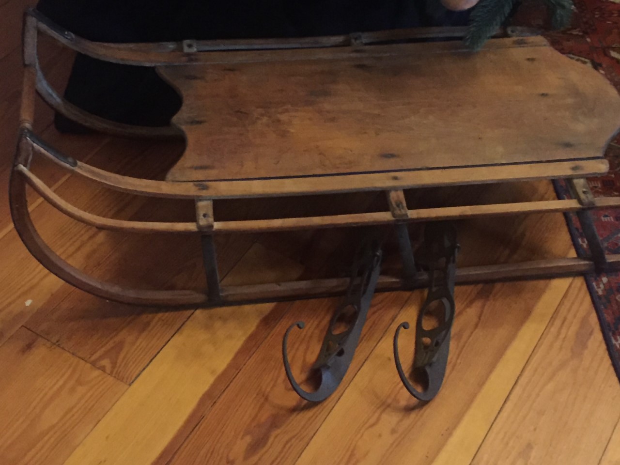 An antique wooden sled. Antique metal ice skates sit below the sled.