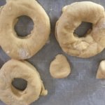 Donut dough shaped into three donuts set atop parchment paper.