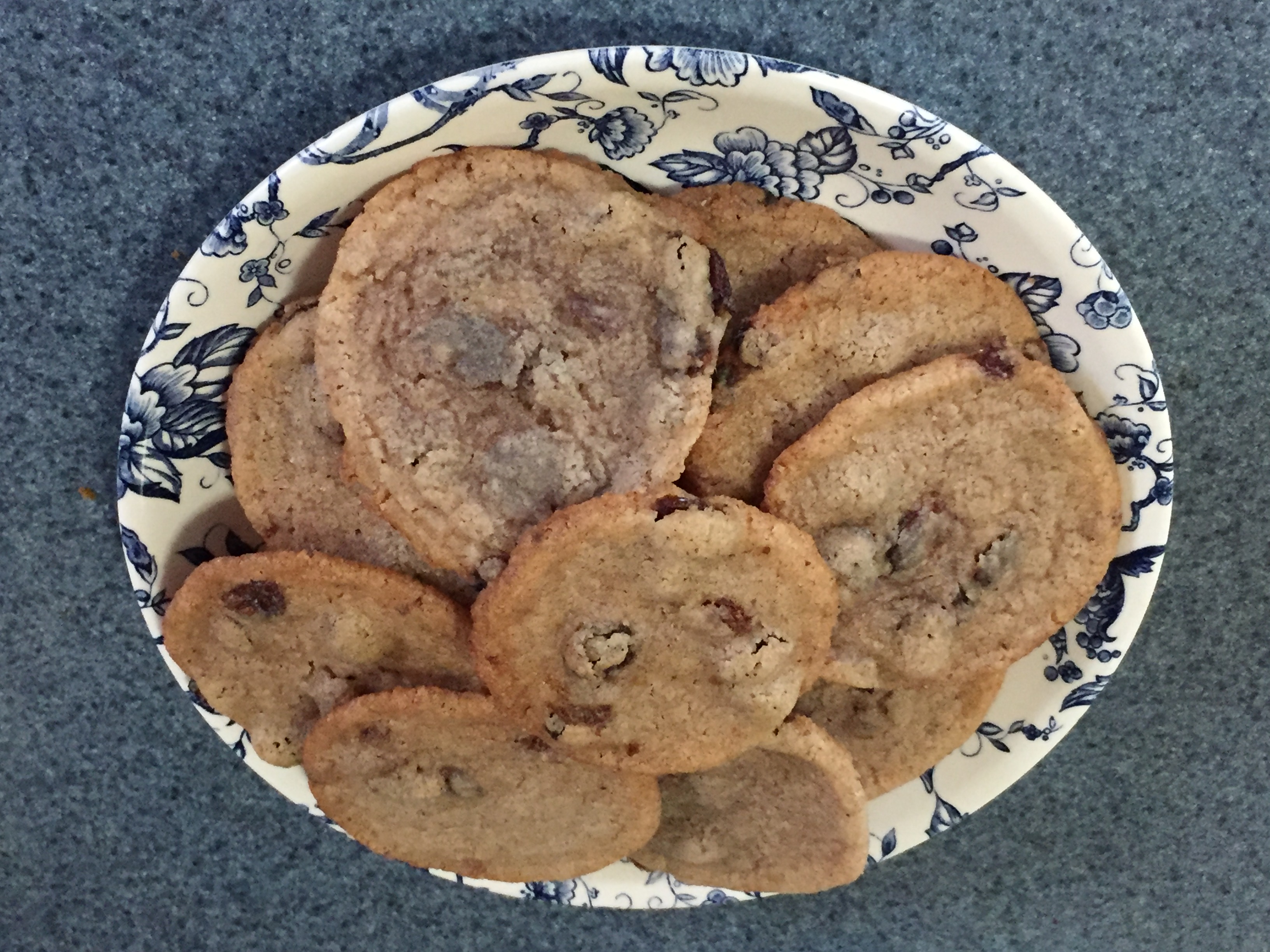A stack of freshly baked raisin cookies on a blue floral china plate.