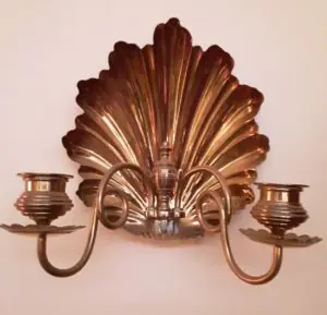 A brass wall sconce witha decorative shell plaque that hangs on the wall. Two curved candlestick arms protrude from it.