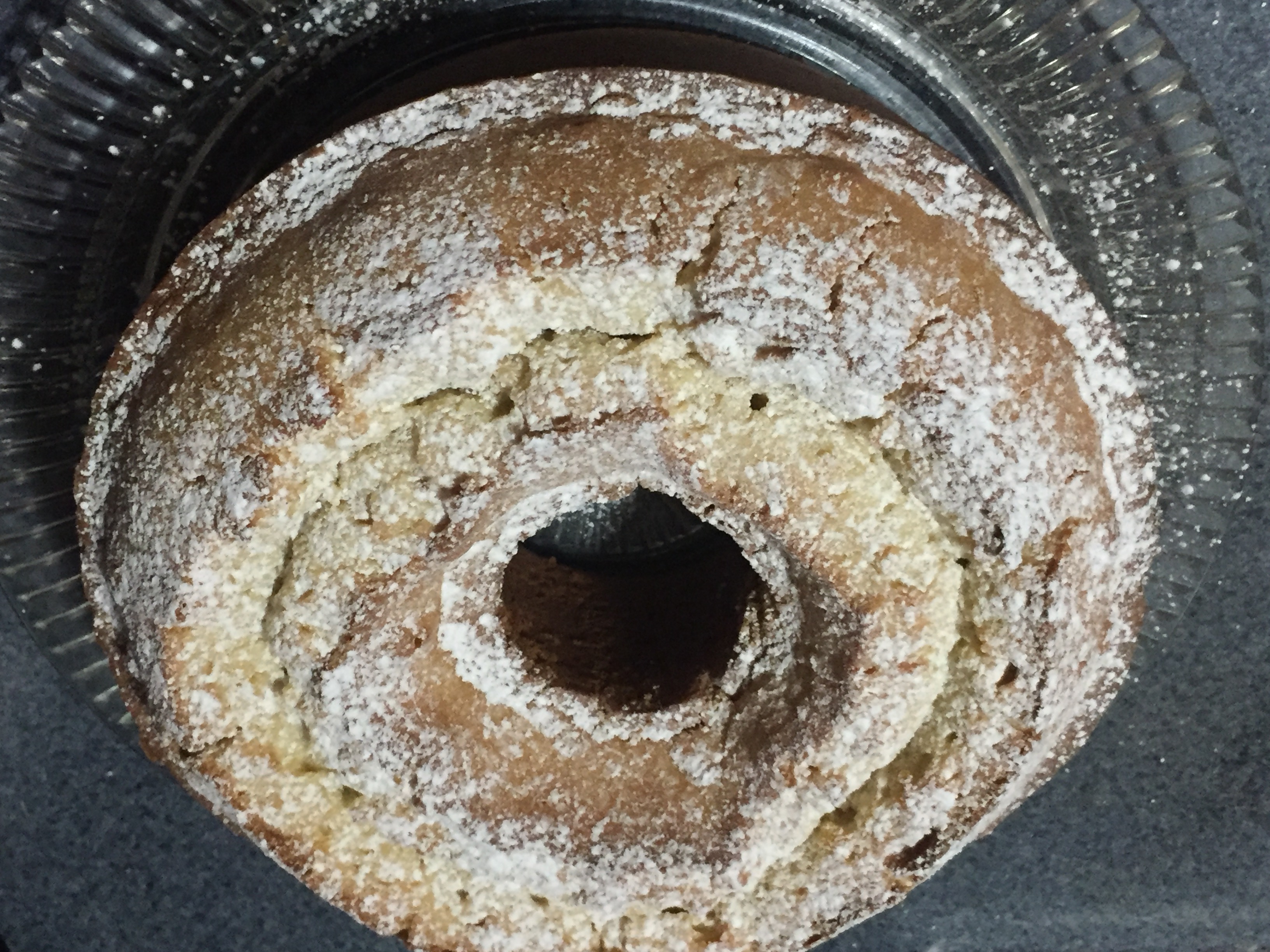 A round cream cake with a hole in its center sprinkled with powdered sugar set on a round glass platter.