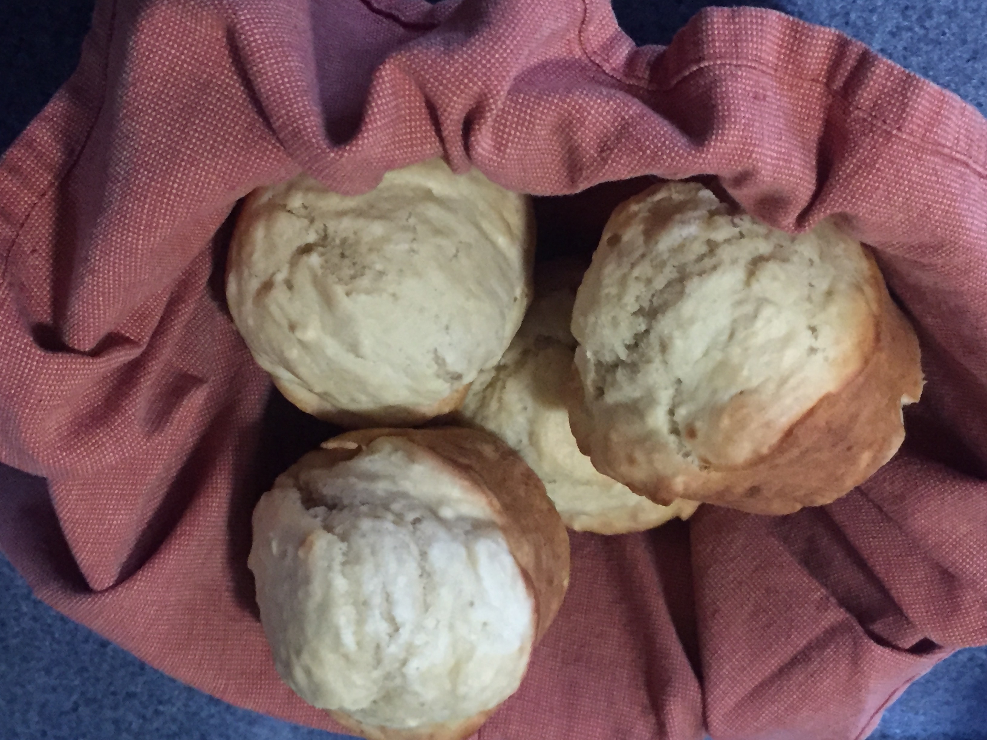 Four freshly baked muffins in a basket lined with a mauve colored cloth napkin.