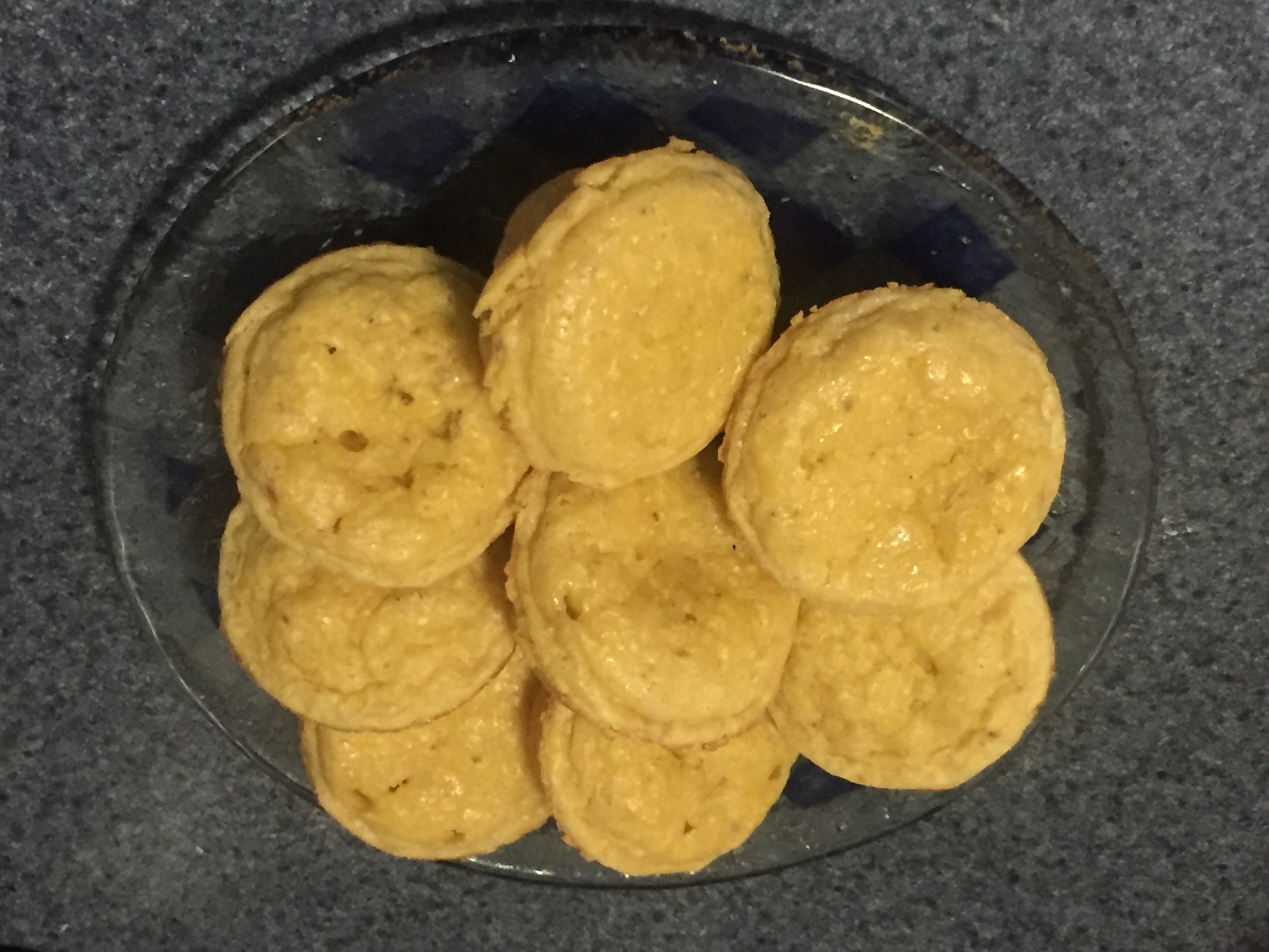 8 small corn muffins on a round clear glass plate with blue check pattern.