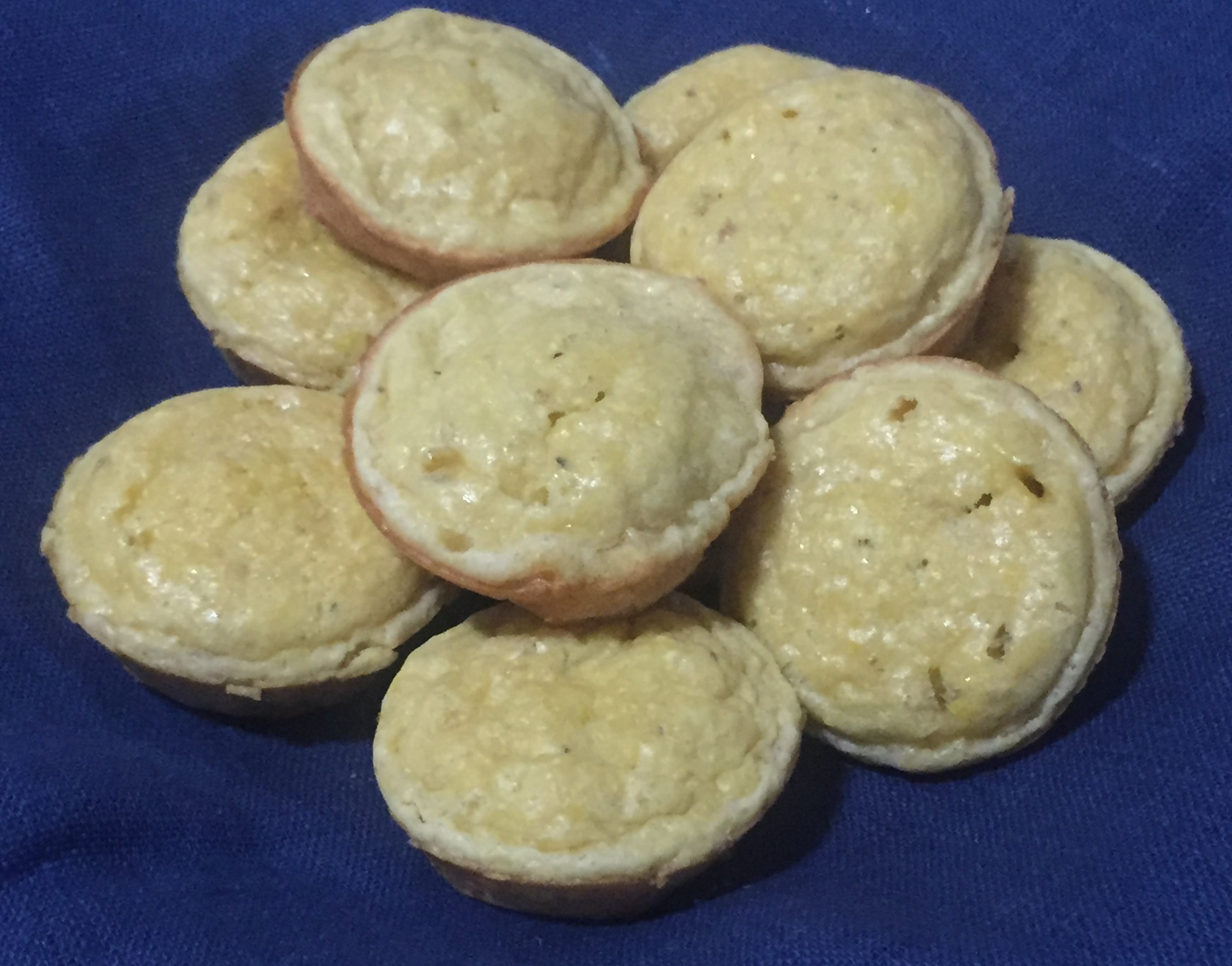 Nine small corn muffins clustered together on a navy blue linen napkin.