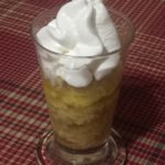 Fresh baked apple pudding in a clear glass tapered parfait cup topped with whipped cream.