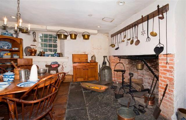 Brick fireplace and cooking hearth with several metal tools including Dutch oven, tin roasting oven, and long-handled tools for cooking.