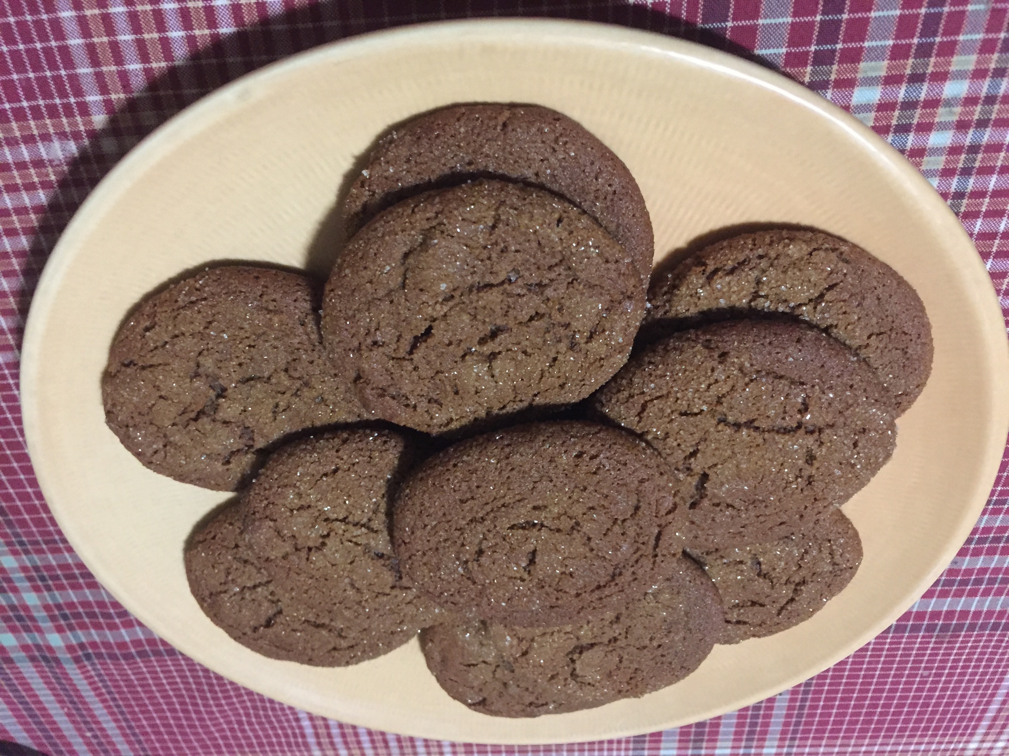 Ten round medium-sized cookies are arranged on a round yellow dish on a red-checked tablecloth.