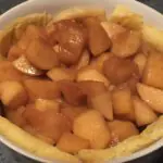 Una fuente de horno llena de corteza de pastelería y trozos de manzana sazonados.