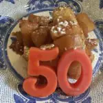 Un postre de crumble de manzana en un plato decorativo. Las velas que forman el número 50 se apoyan en el postre.