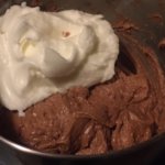A metal mixing bowl full of brown cake batter and whipped cream.