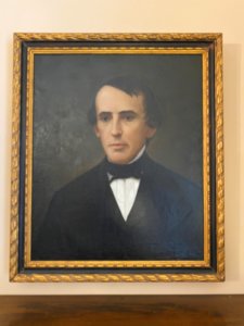 Painted portrait of Jacob Miller. A middle-aged white male dressed in black suit and tie with white shirt looks to the left.