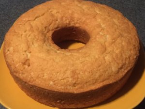 A round baked cake with a hole in the middle sits on top of a yellow plate.