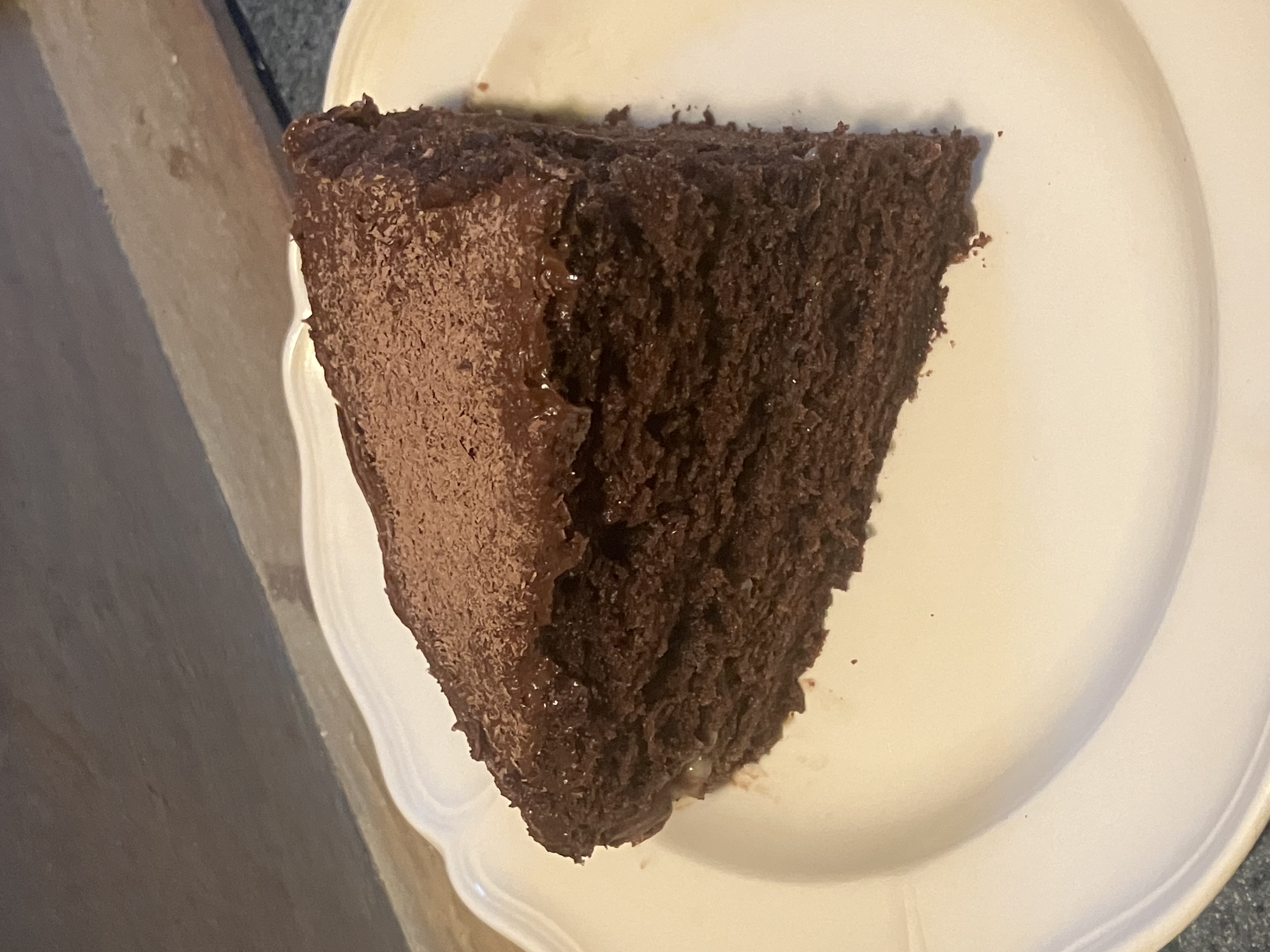 Slice of chocolate layer cake with frosting and shaved chocolate on a white plate.