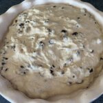 Nameless cake batter with raisins in a round scalloped baking dish.
