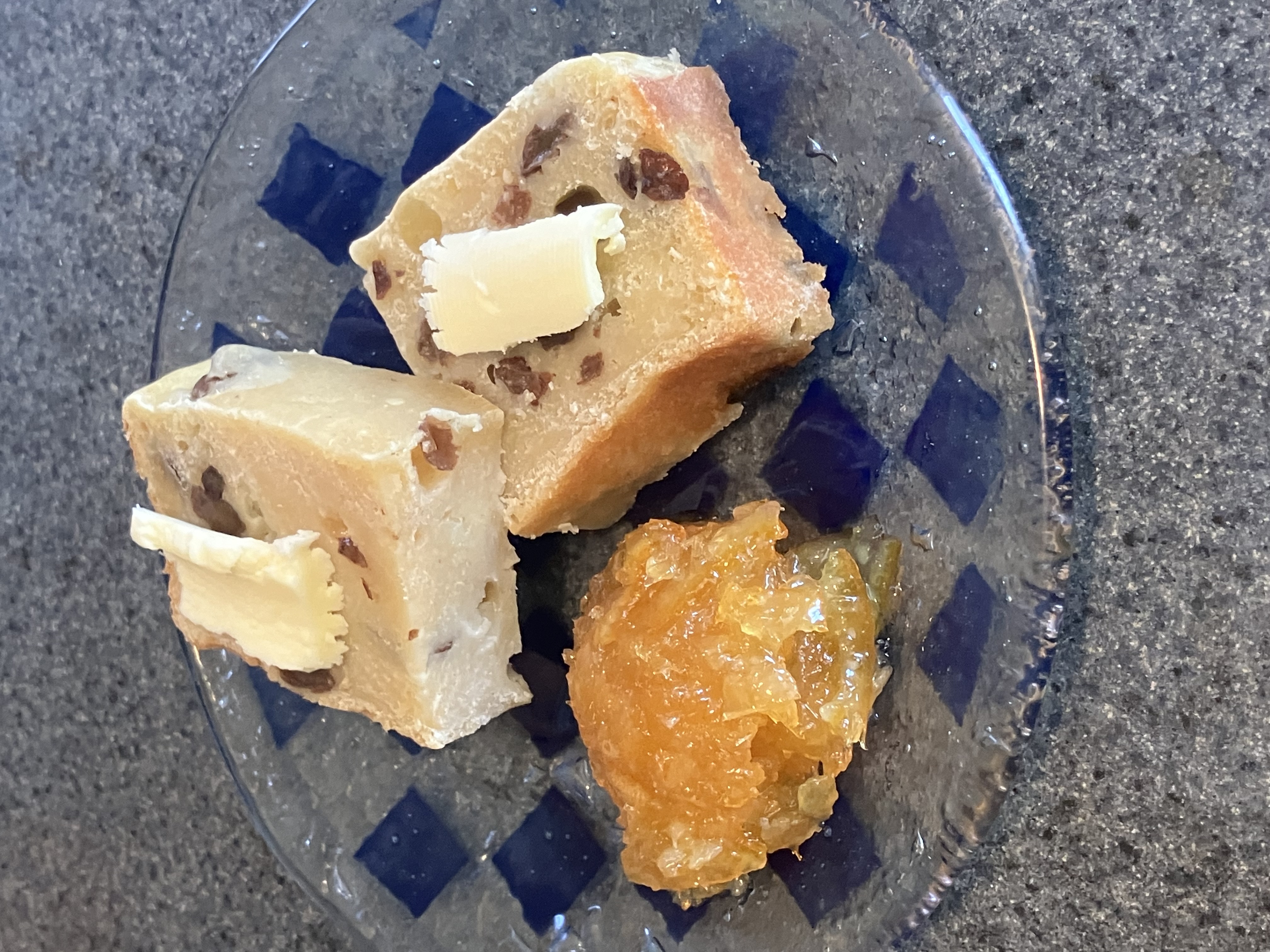 Square slice of baked Nameless cake with raisins with butter on top. There is some orange marmalade to the left of the slices.