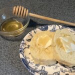 Two slices of cake with butter and honey on top. A bowl of honey and honey dipper are behind the cake.