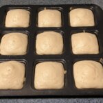 A square baking pan with 9 square openings with baked tea cakes.