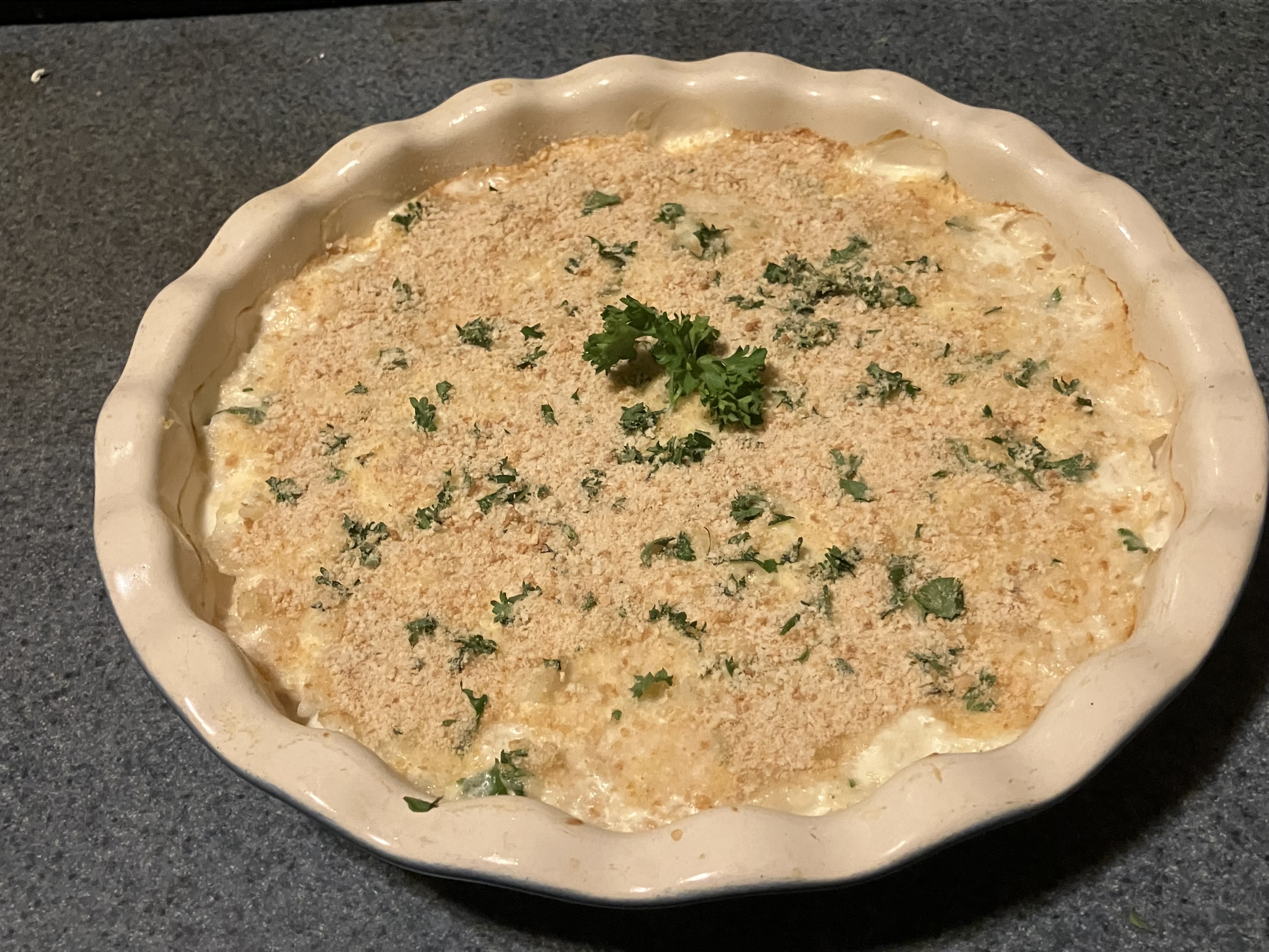 A round baking dish with baked fish pudding topped with bread crumbs and parsley.