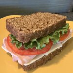 A sandwich with bread, lettuce, tomato, meat, and cheese on top of a yellow plate.