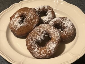 Four baked doughnuts arranged on a plate and topped with powdered sugar.