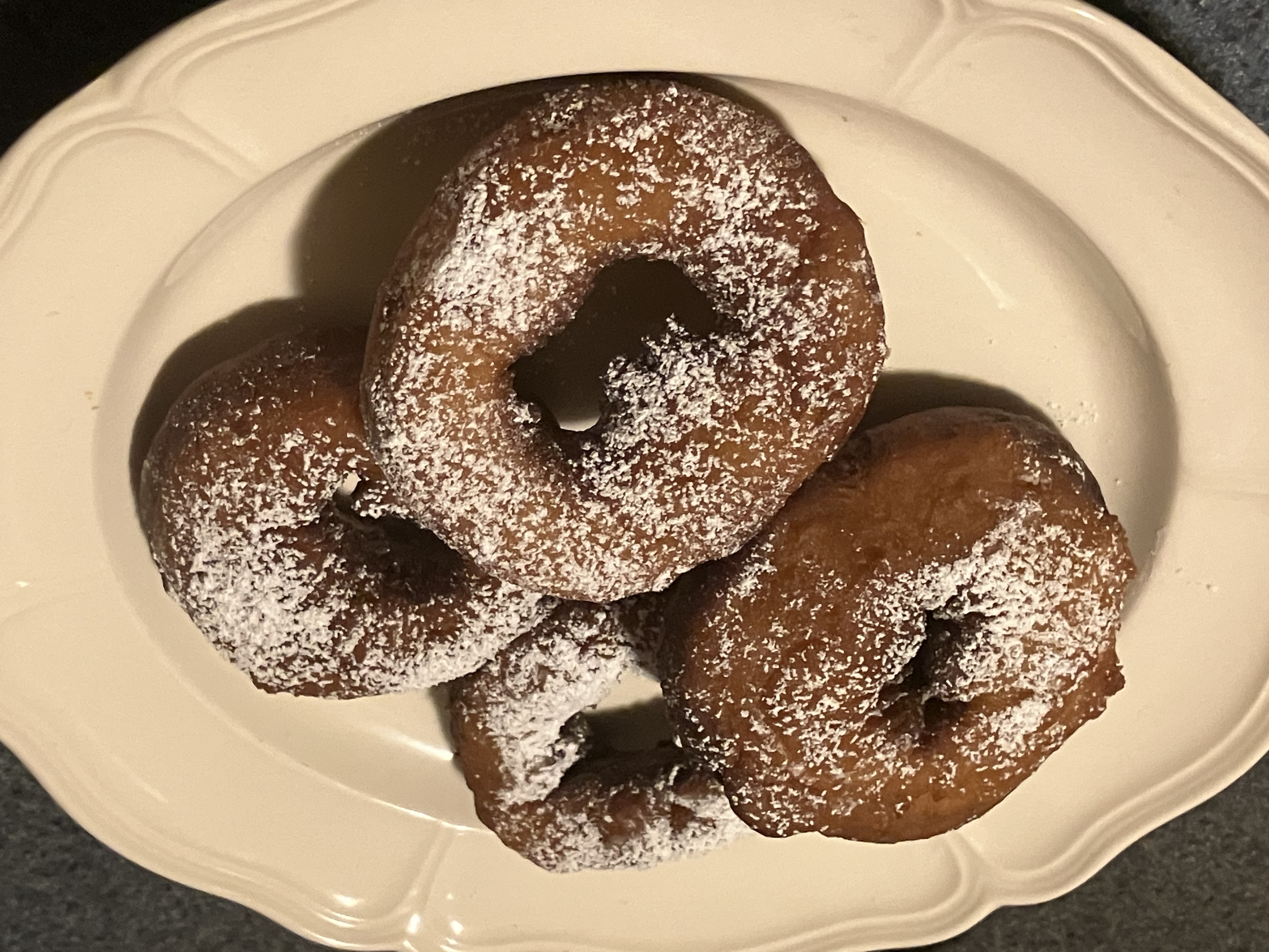 Four baked doughnuts arranged on a plate and topped with powdered sugar.