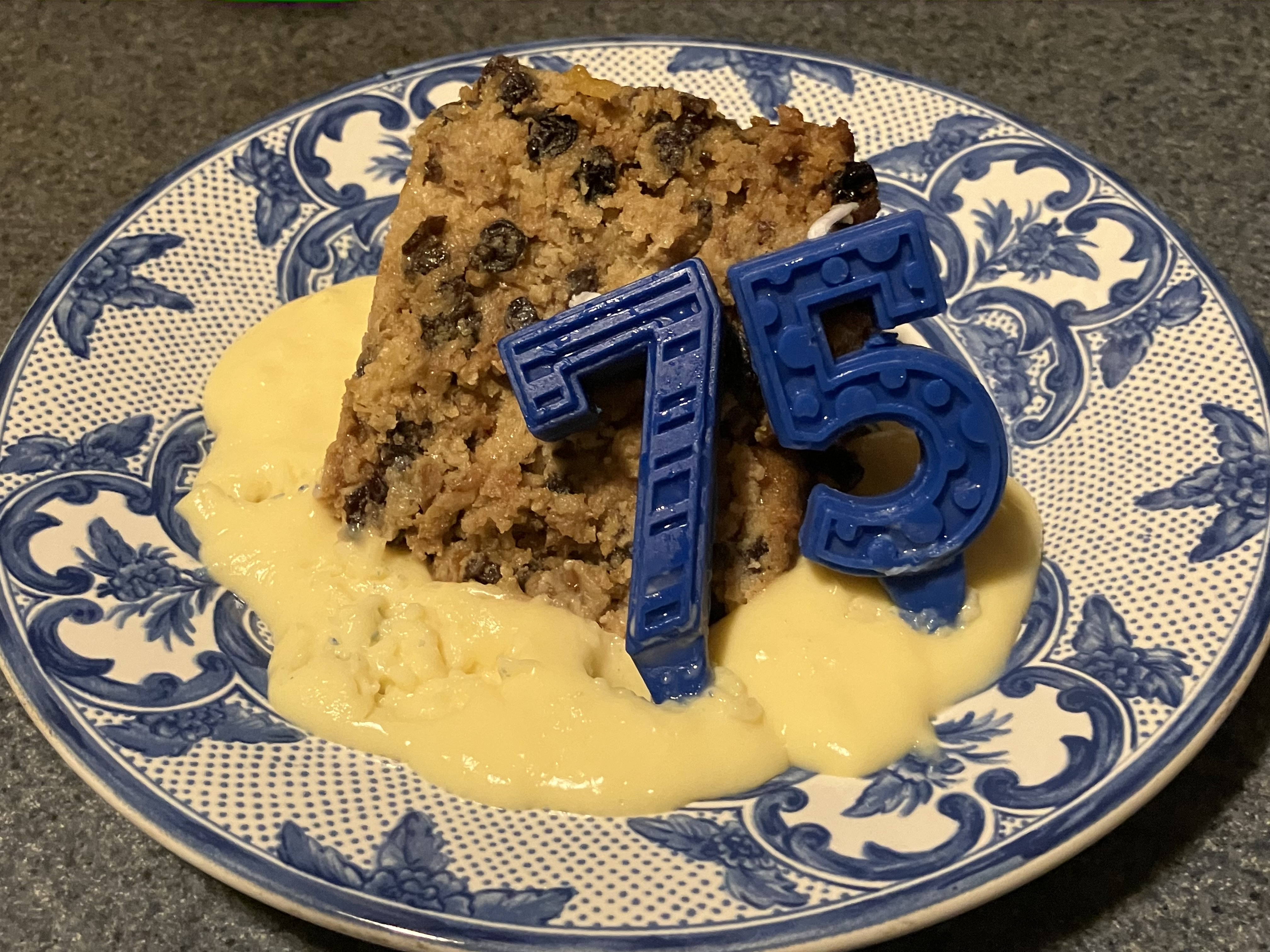 A slice of baked chancellor pudding on top of cream with blue 75 candles.