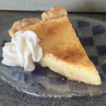 A baked slice of Lemon Pie sits on a plate with whipped cream.