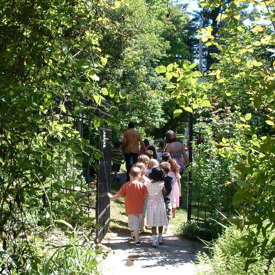Several children and adults walk through an open gate into a garden.